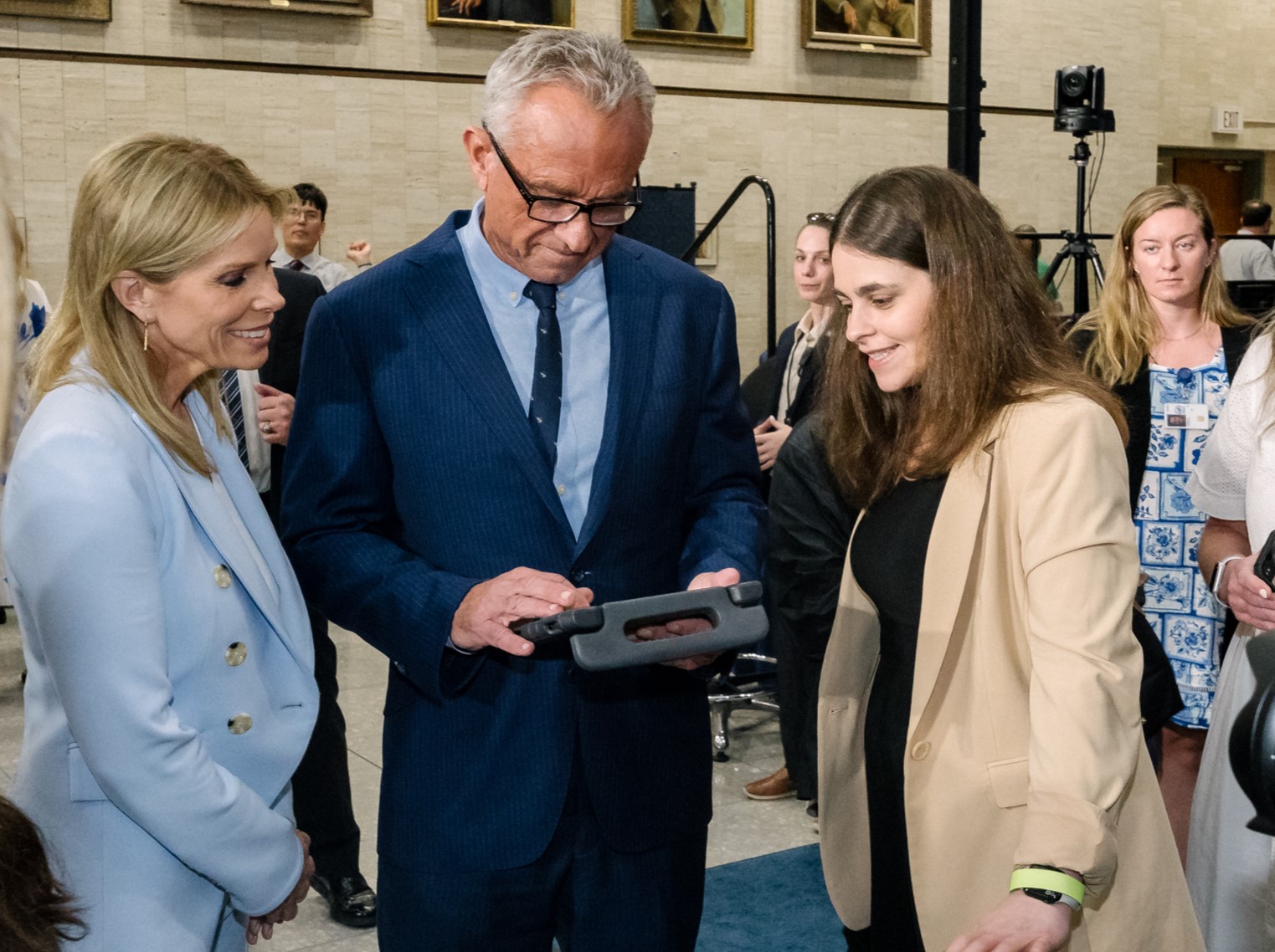 Consultant and disability advocate Jordyn Zimmerman shows her communication device to HHS Secretary Robert F. Kennedy, Jr. and Cheryl Hines